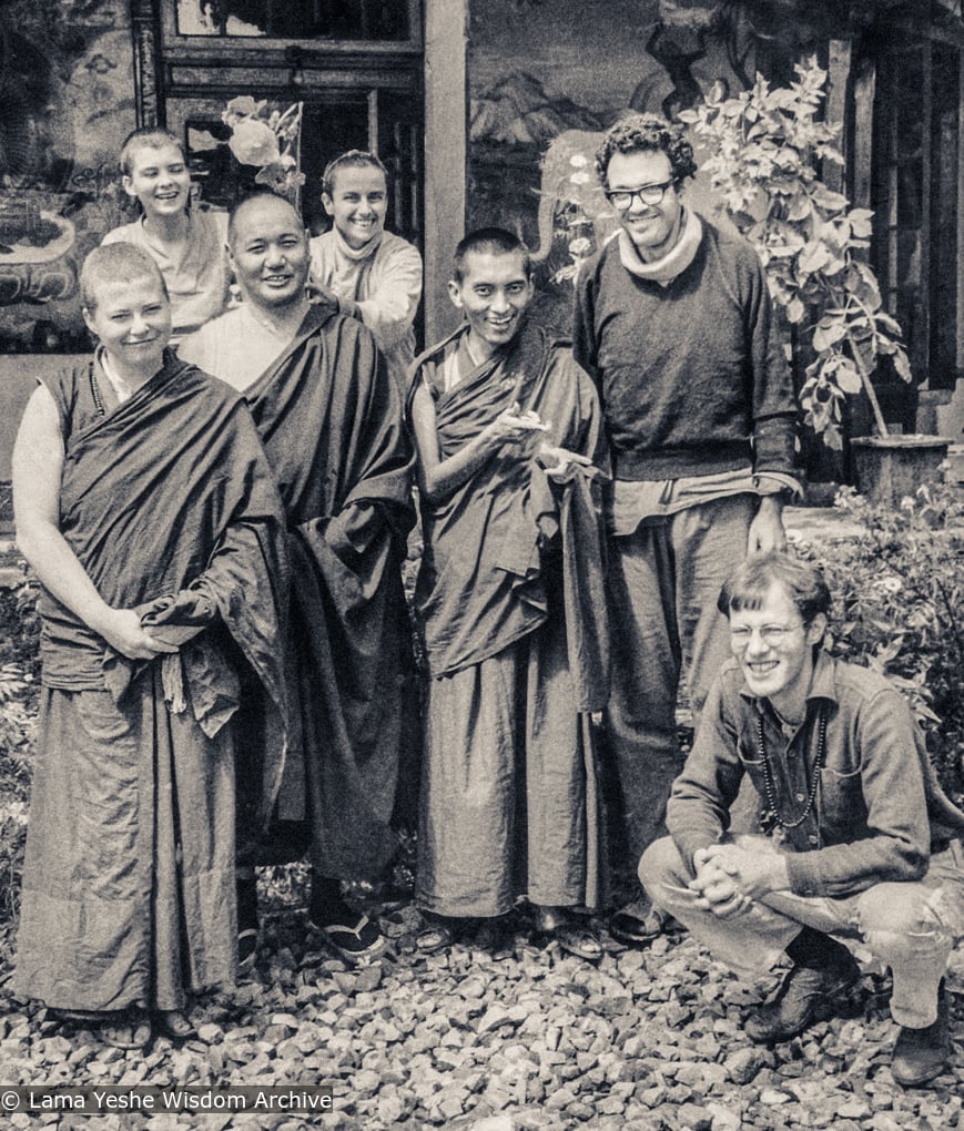 (18950_pr-3.psd) Lama Yeshe and Lama Zopa Rinpoche with students and artists, Tushita Retreat Centre, Dharamsala, India, 1973. Wim (squatting at the front right), the Dutch artist, who had painted the walls of Lawudo Gompa the year before, arrived at Tushita and painted a mural of Guru Shakyamuni on the left front porch wall of the building, while Lawrence Greenberg (standing to the right of Rinpoche) painted the four friends on the right. Suzanne Lee is standing to the left of Lama Yeshe.