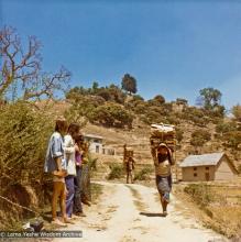 (13298_pr-2.psd) Villagers carrying wood while westerners watch, road to Kopan Monastery, Nepal, 1973. The monastery is on the hilltop to the right. Photo by Christine Lopez.